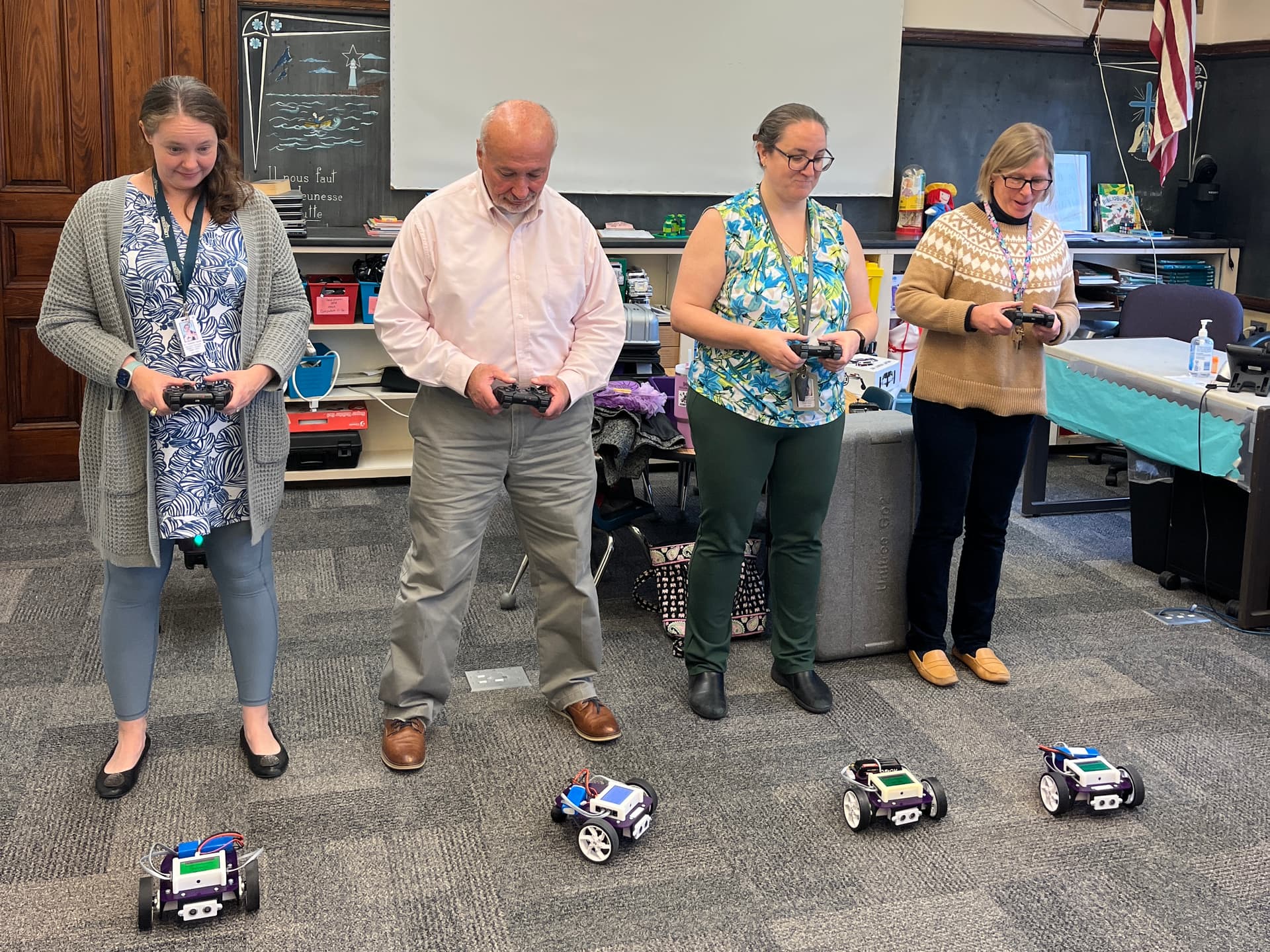 Four teachers drive Axle robots with game controllers across a classroom carpet during a demo