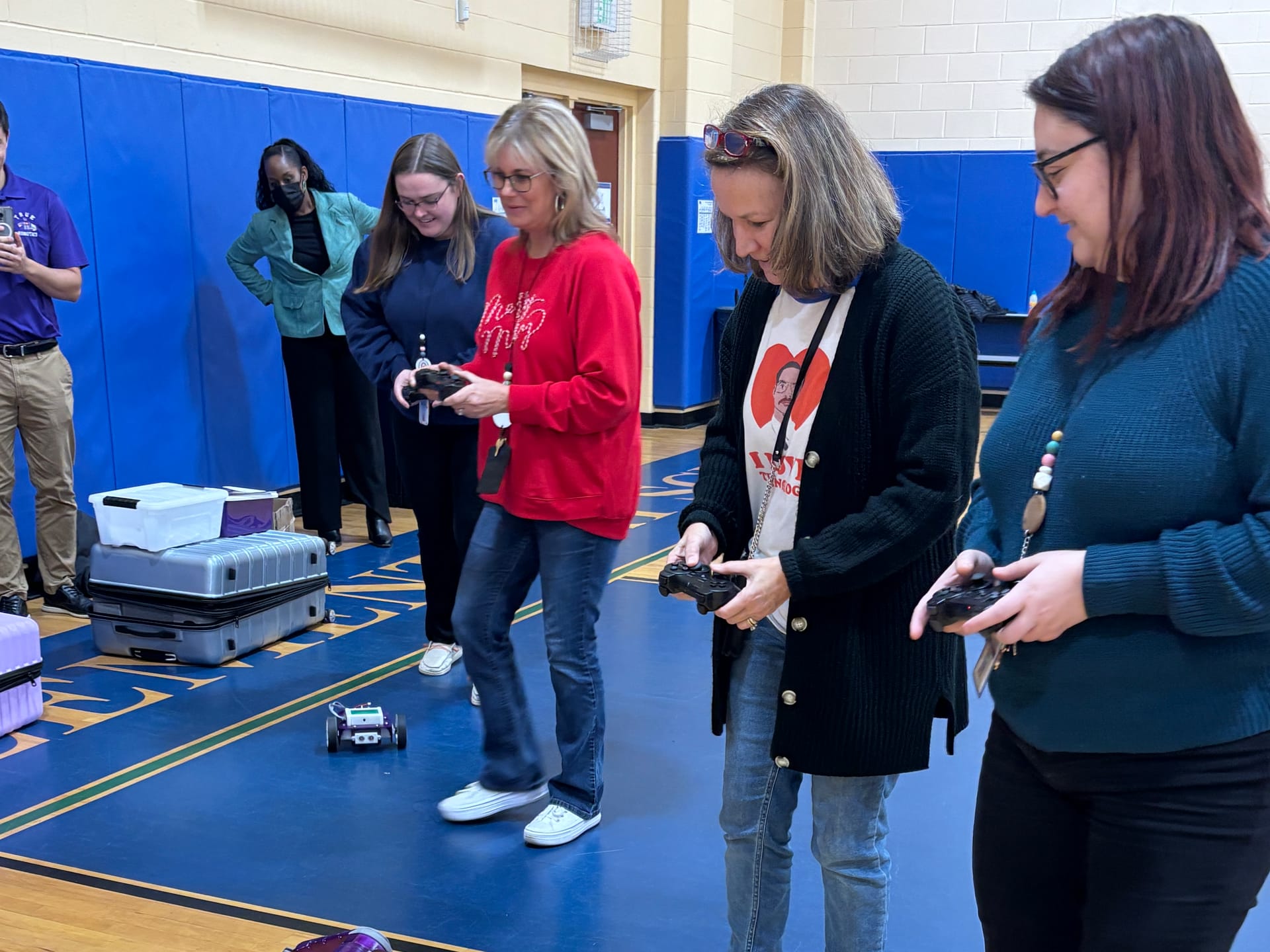 Teachers try driving a Pilot robot with game controllers on the gym floor during a school visit