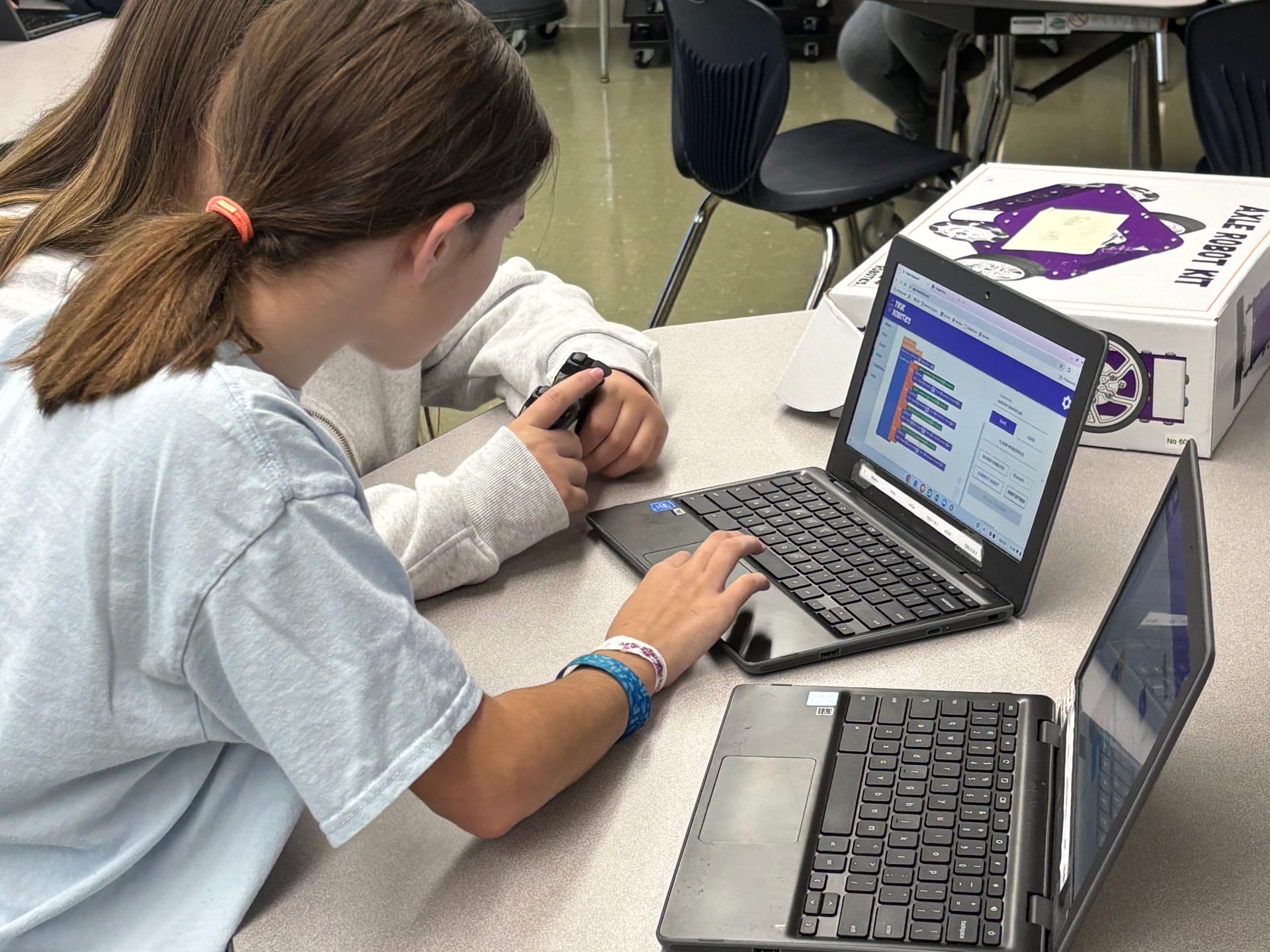 Two middle school students program on Chromebooks running True Robotics Playground next to an Axle Robot Kit box