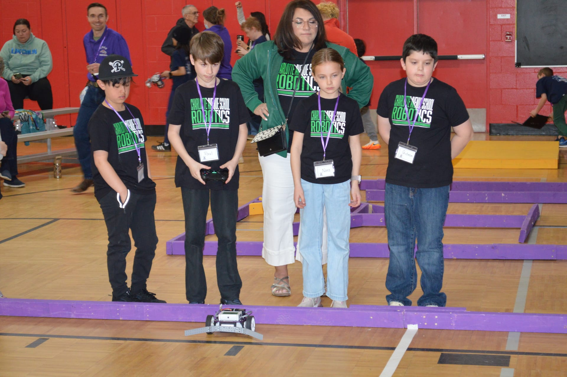 A team of students with game controllers drives their robot along the purple-walled course
