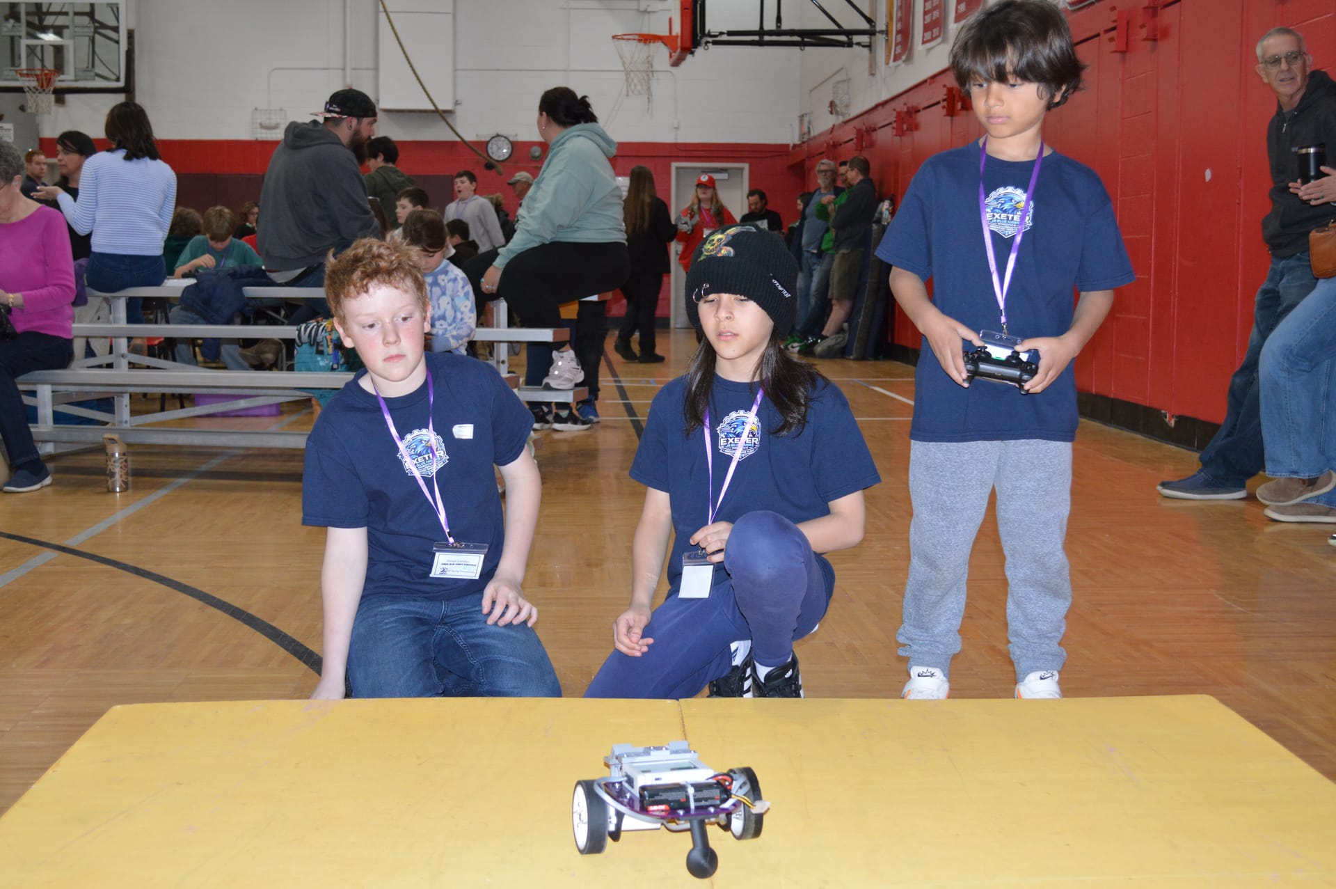 Three students watch their Pilot robot with FlexForge attachments cross the yellow ramp, one holding a game controller