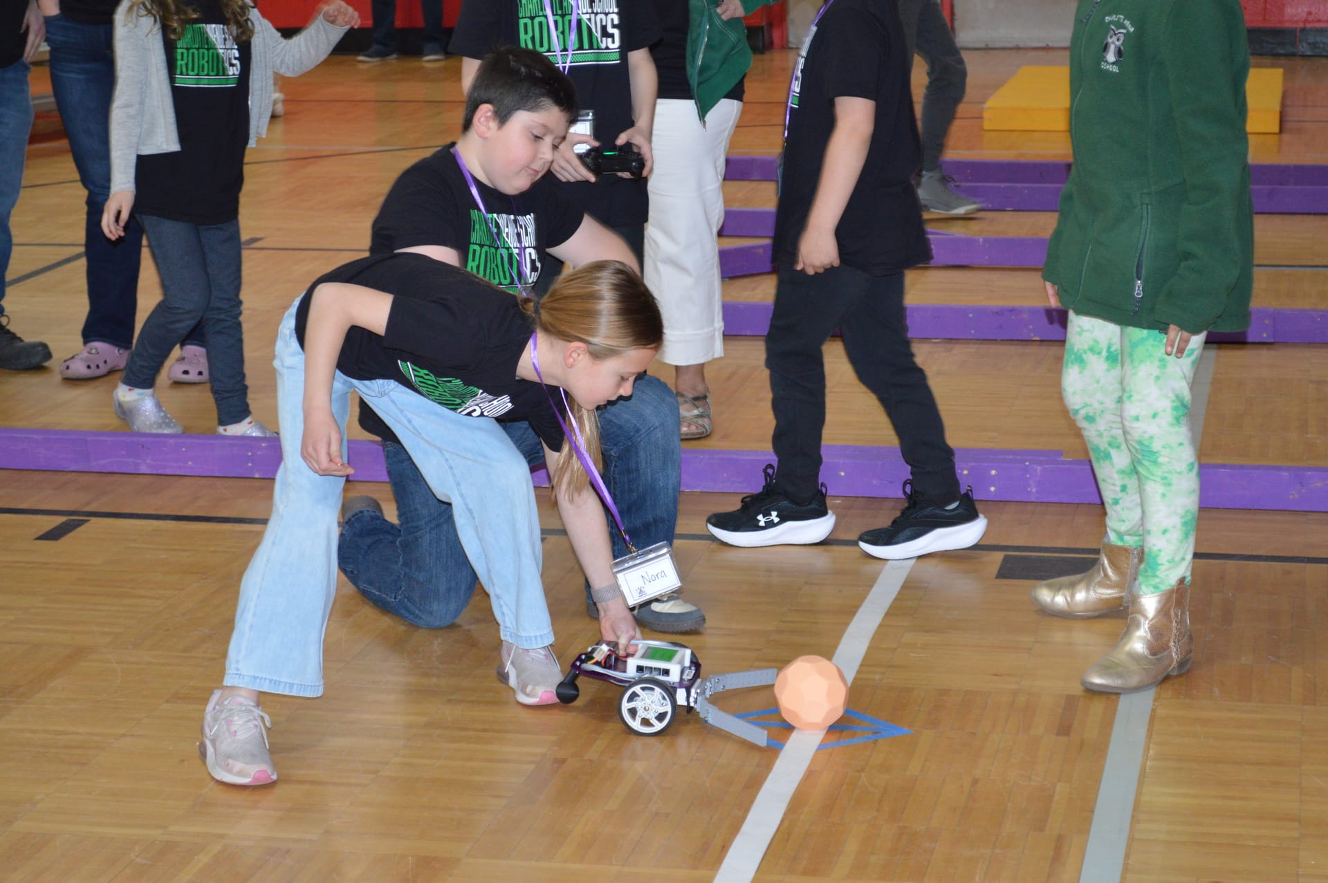 A student sets a Pilot robot with a FlexForge scoop on the course line beside the ball as teammates look on