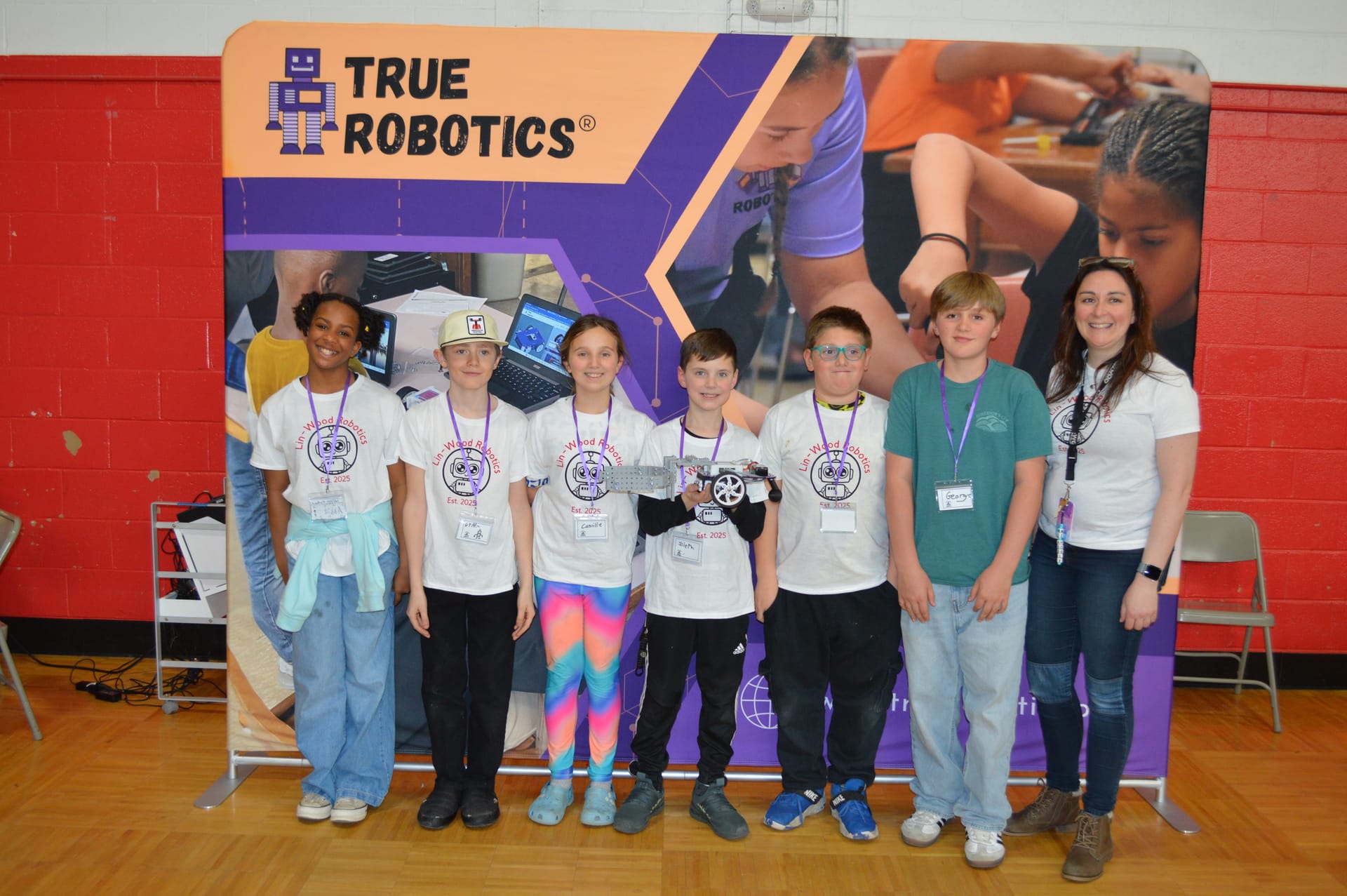 A team poses with their Pilot robot in front of the True Robotics backdrop at the competition