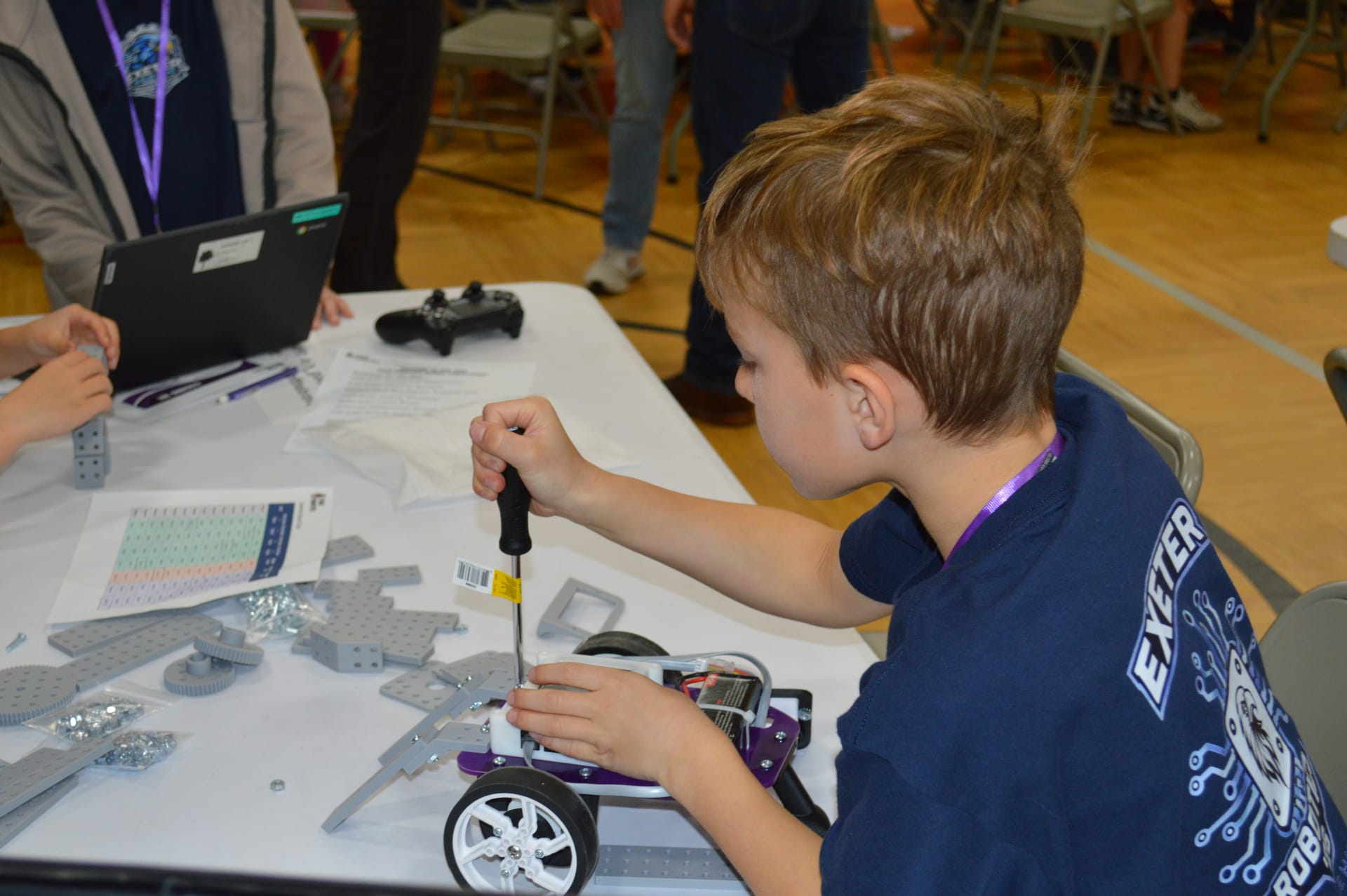 A student drives a screw into a FlexForge beam on a Pilot robot with a Chromebook open nearby