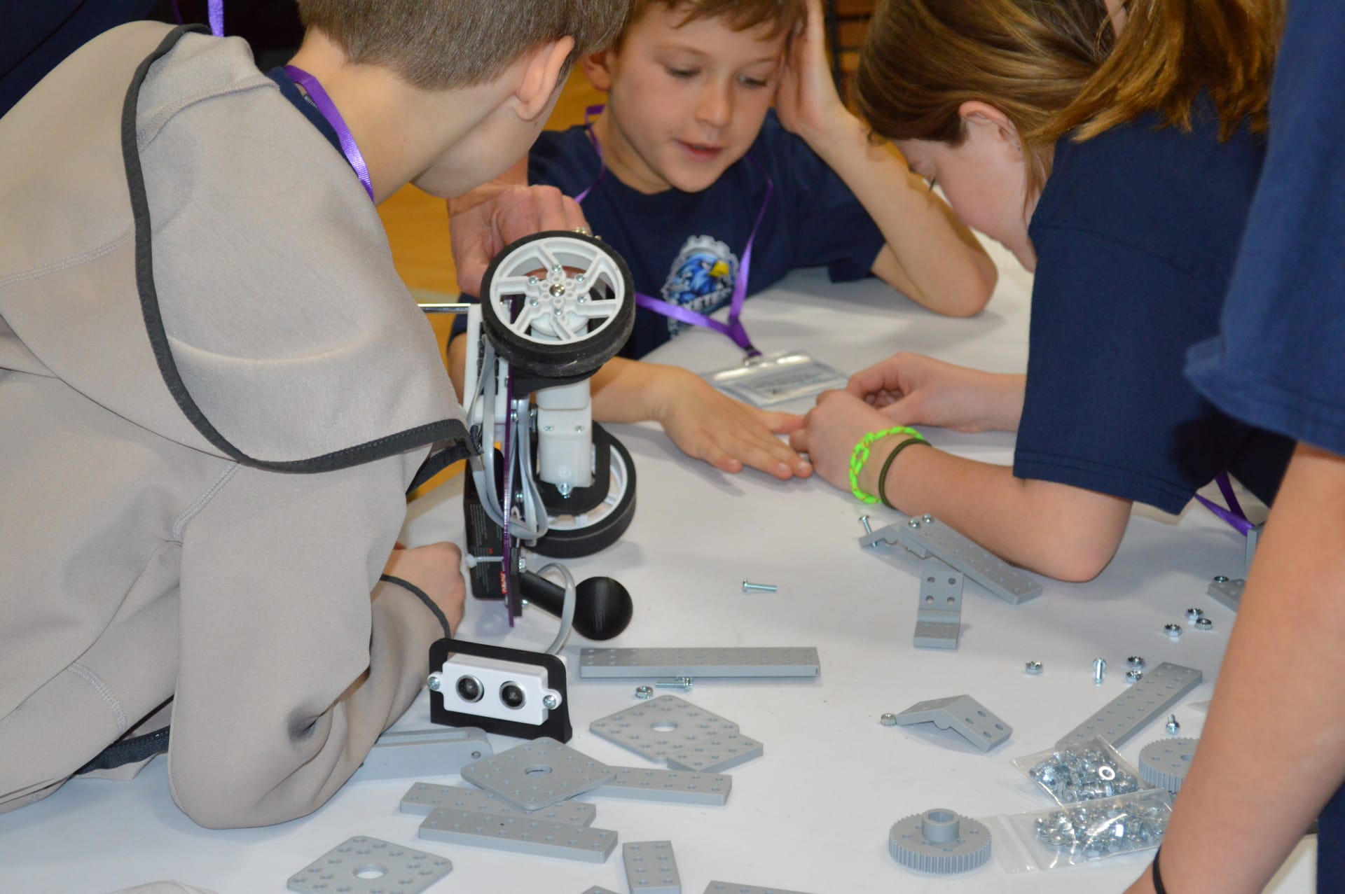 Close view of students' hands fitting FlexForge beams around a robot wheel
