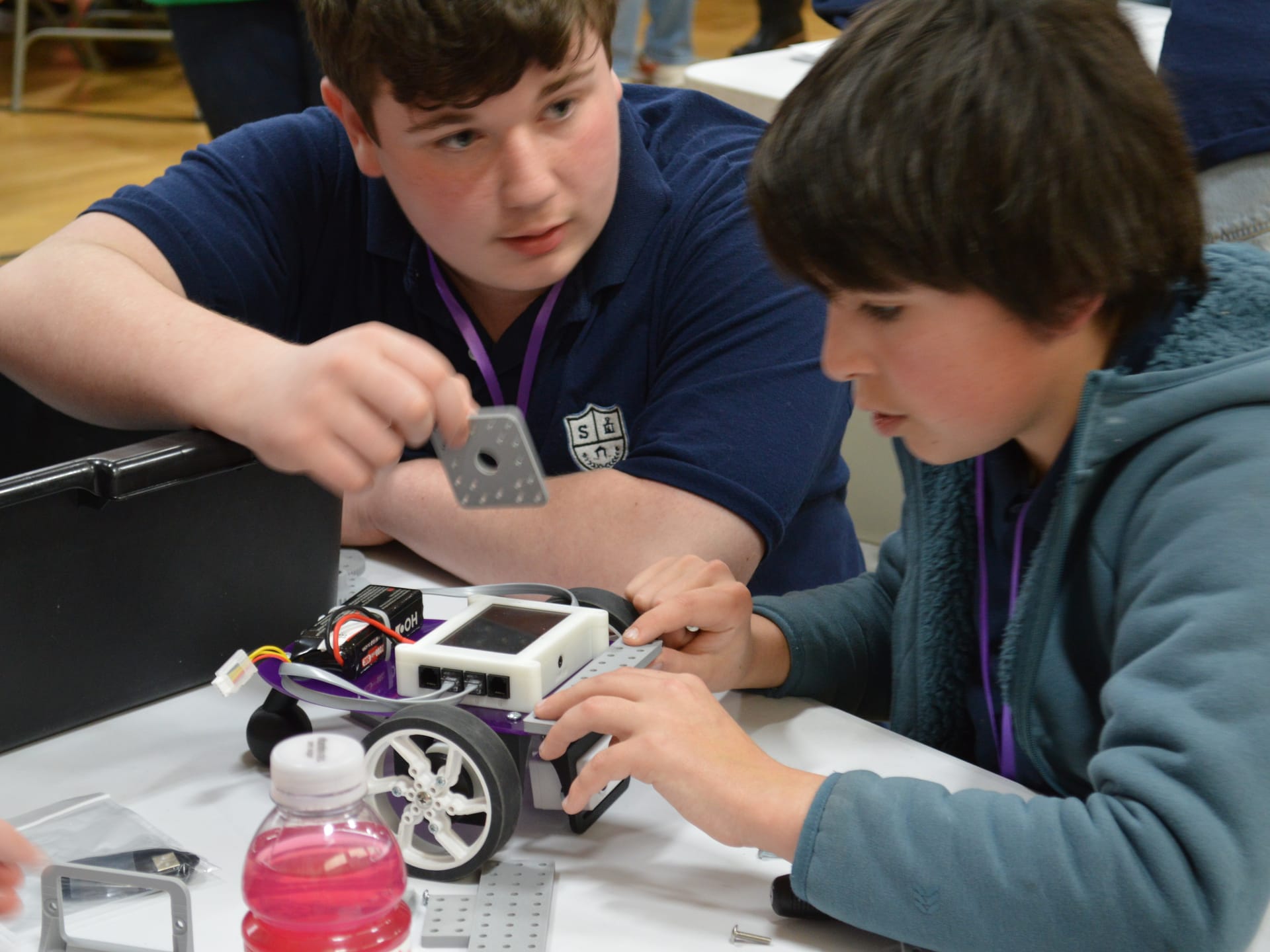 Two students hold a FlexForge plate over a Pilot robot while deciding where to mount it