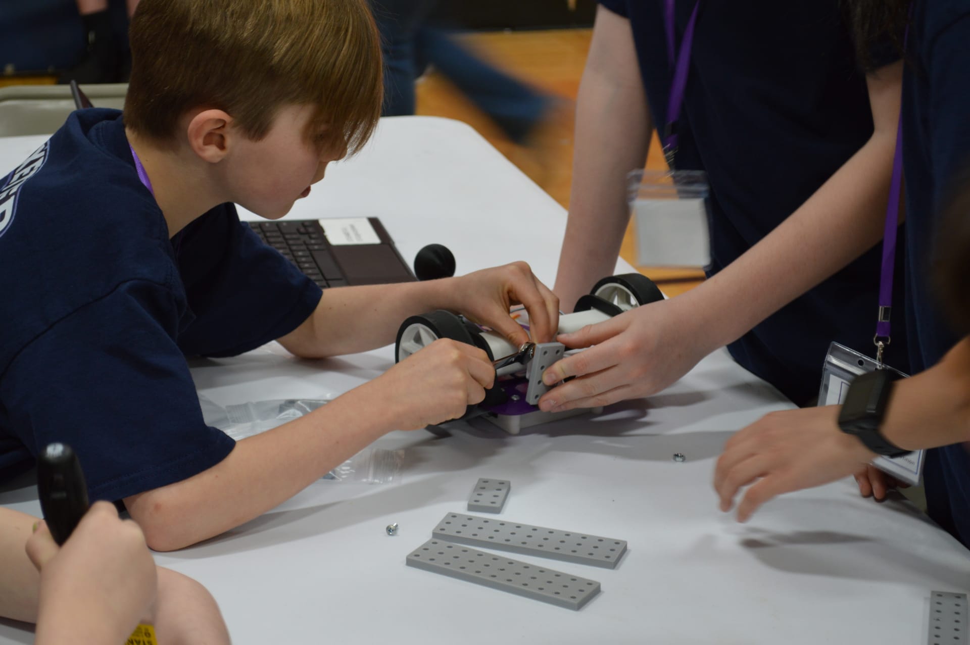 A student attaches a FlexForge bracket to a robot with gray beams laid out on the table