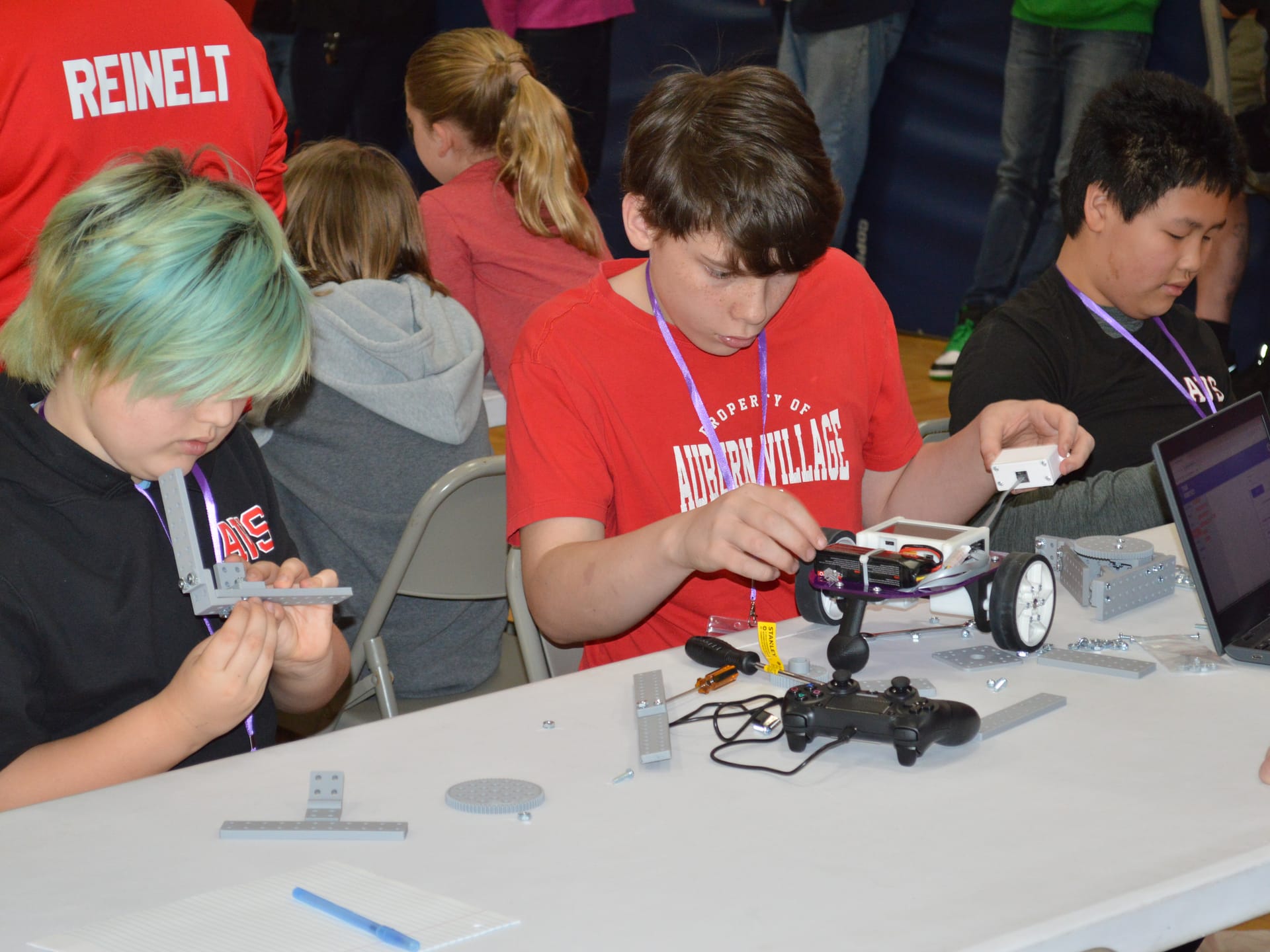Two students bolt FlexForge beams onto a Pilot robot at a competition table with a game controller and Chromebook beside them