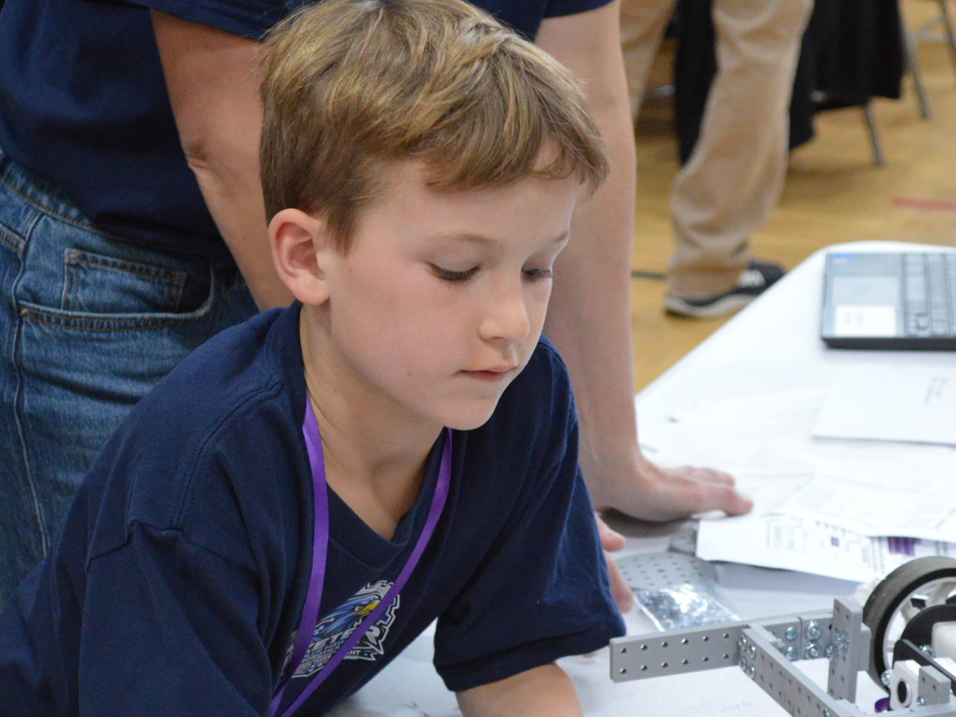 A student leans over a competition build table with FlexForge beams and a laptop beside him