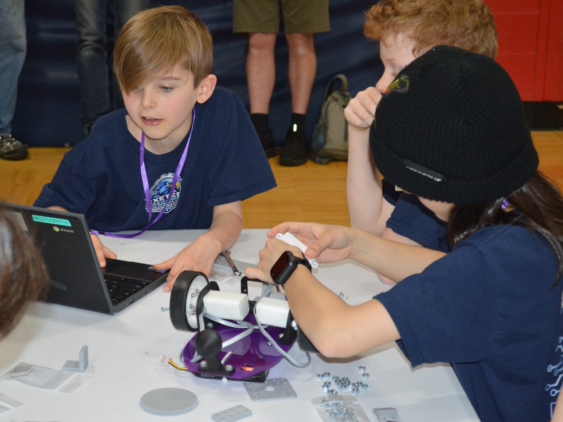 Two students attach FlexForge parts to a Pilot robot at a competition table with a Chromebook open beside them