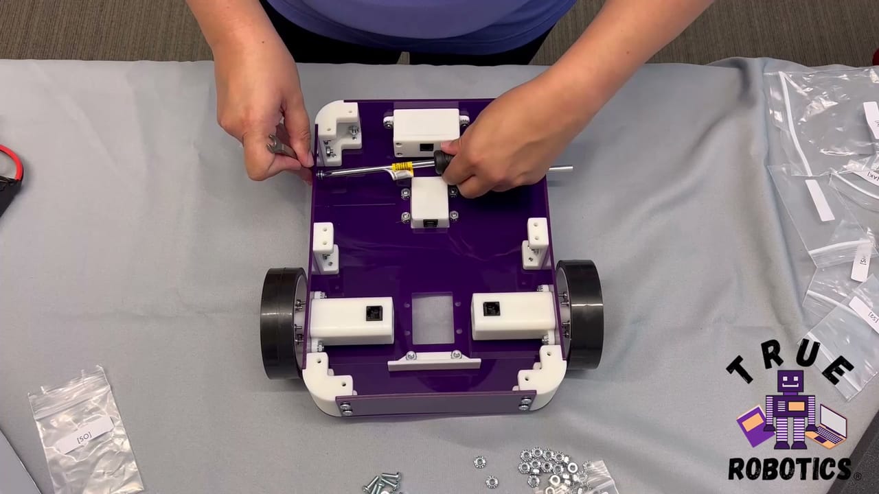 Hands fit a wheel to a part built Axle Robot Kit beside loose screws and a screwdriver