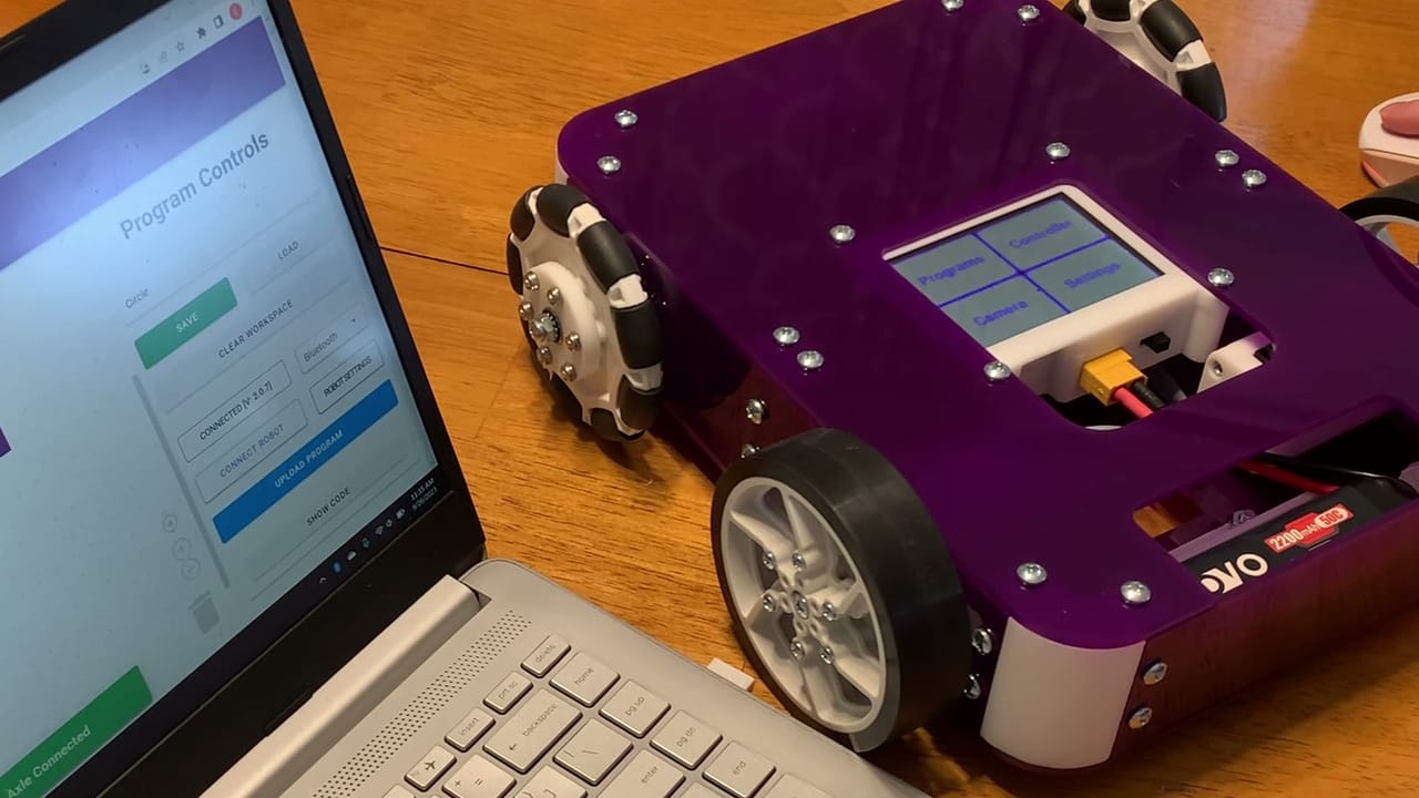 A built Axle Robot Kit with its touchscreen menu lit sits on a table beside a laptop running True Robotics Playground