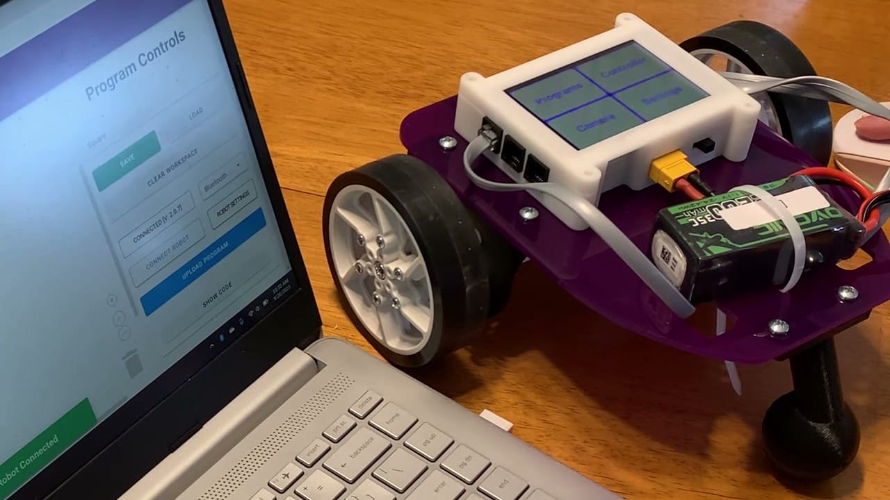 A built Pilot Robot Kit with its touchscreen menu lit sits on a table beside a laptop running True Robotics Playground