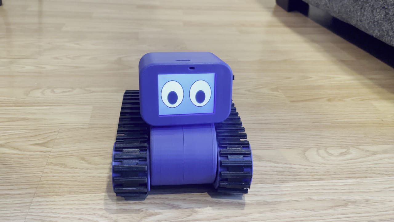 The Treads Robot faces the camera on a wood floor with two cartoon eyes on its screen